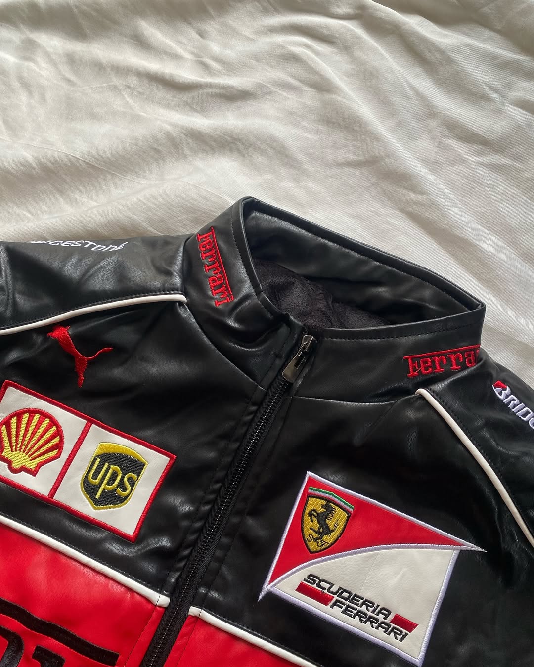 Black leather racing jacket with red side stripe and sponsor patches near the zipper