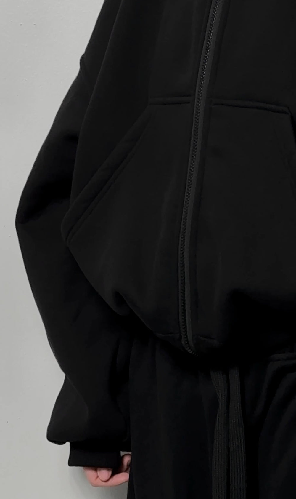 Black balaclava zip-up hoodie close-up with central zipper and front pouch detail.