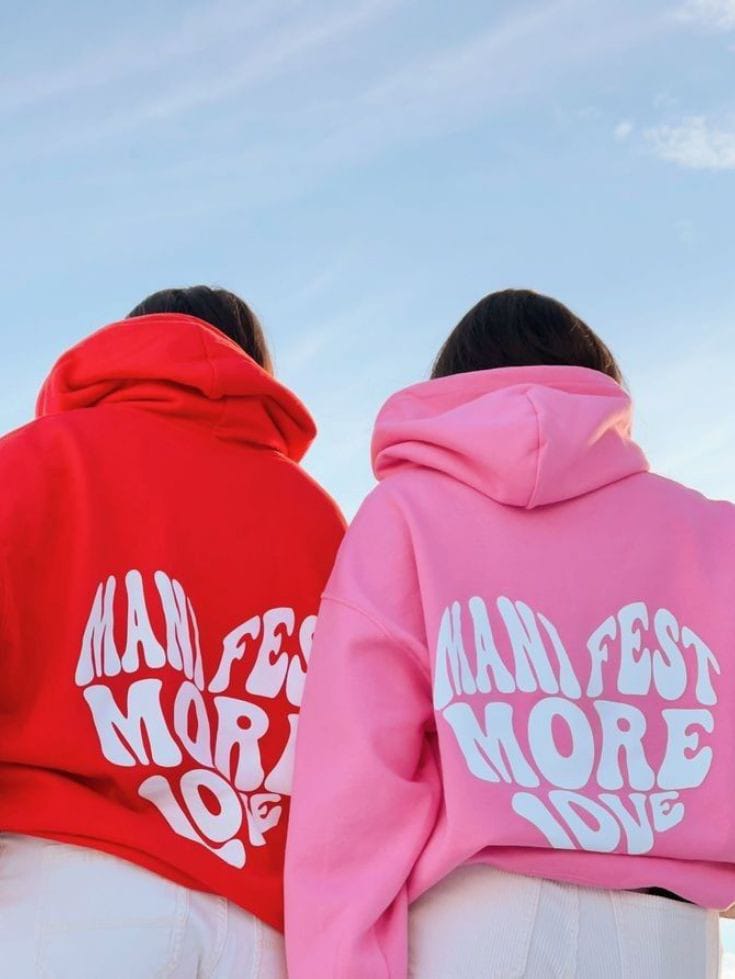 Red and light pink cotton couple hoodies with bold 'MANIFEST MORE LOVE' print on back