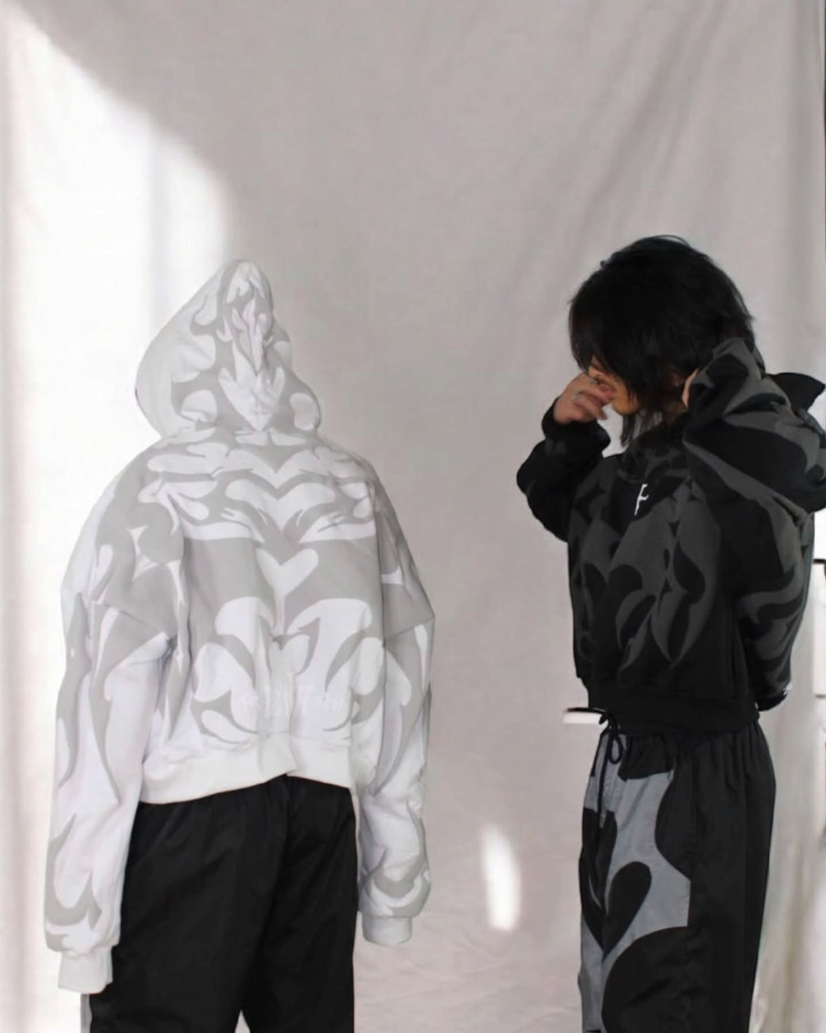 White and black pullover hoodies with light tribal prints, both with hood drawstrings