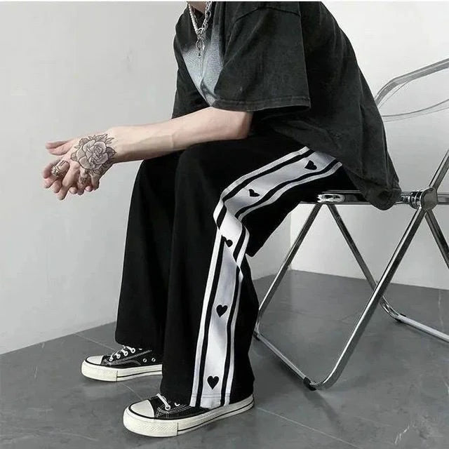 Black baggy track pants with white side stripe and heart print, wide legs
