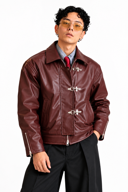 Side angle of a men's burgundy leather-look jacket with silver buckle detailing, structured collar and zippered cuffs.