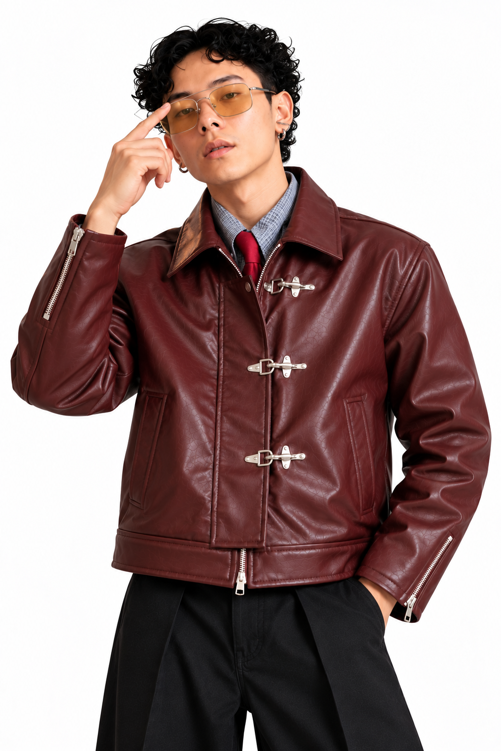 Model seated on a chair wearing Mercywear burgundy leather-look jacket with vintage metal clasps and black trousers.